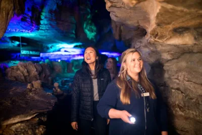 a guide with a flashlight leads a woman through a cave 