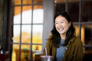 A smiling woman sits in front of a window 