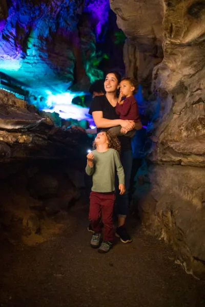 A woman carries a child and follows another child through a cave 