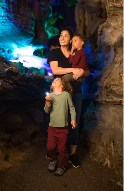 A woman carries a child and follows another child through a cave 