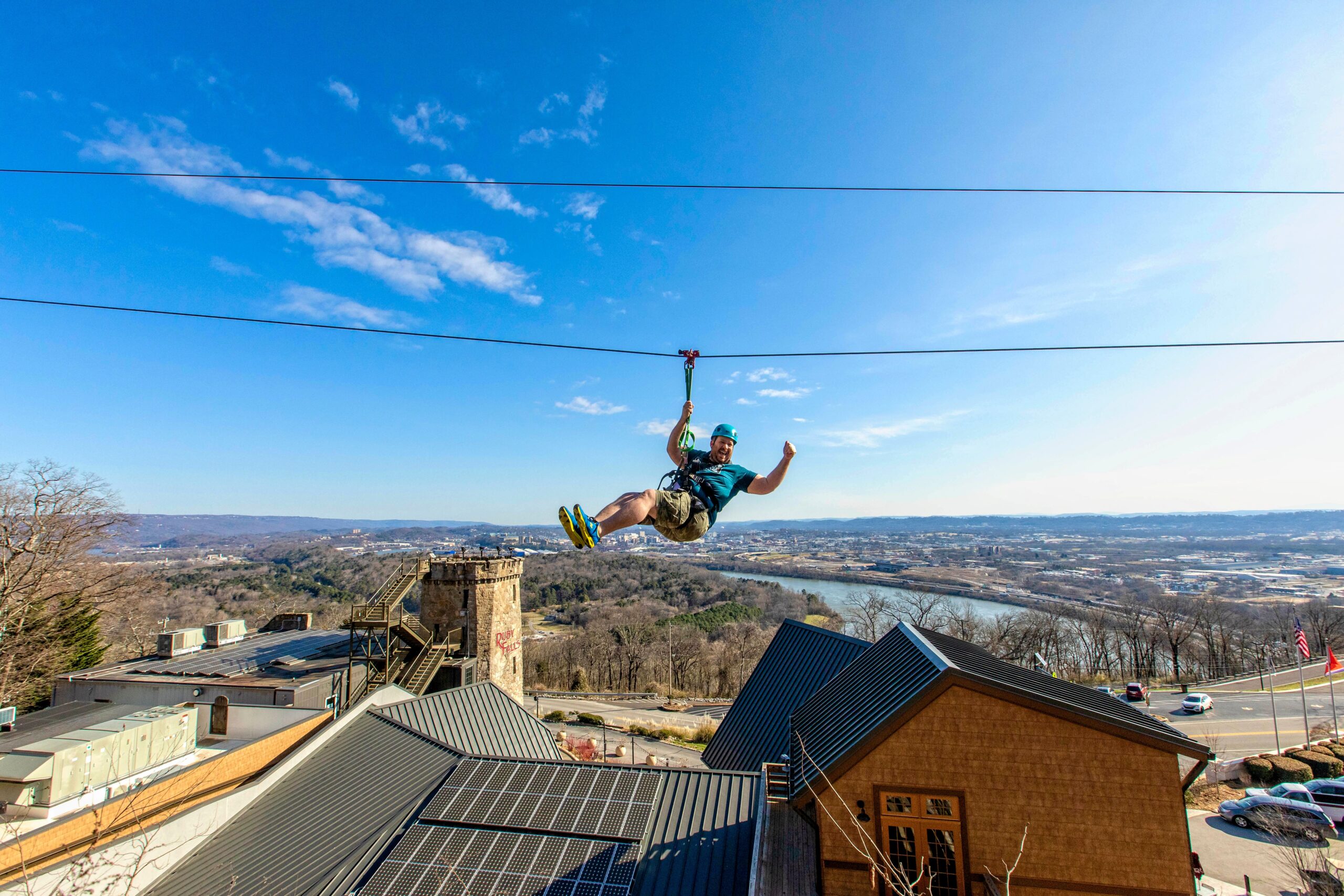 A man enthusiastically rides the zip line and raises a fist in excitement