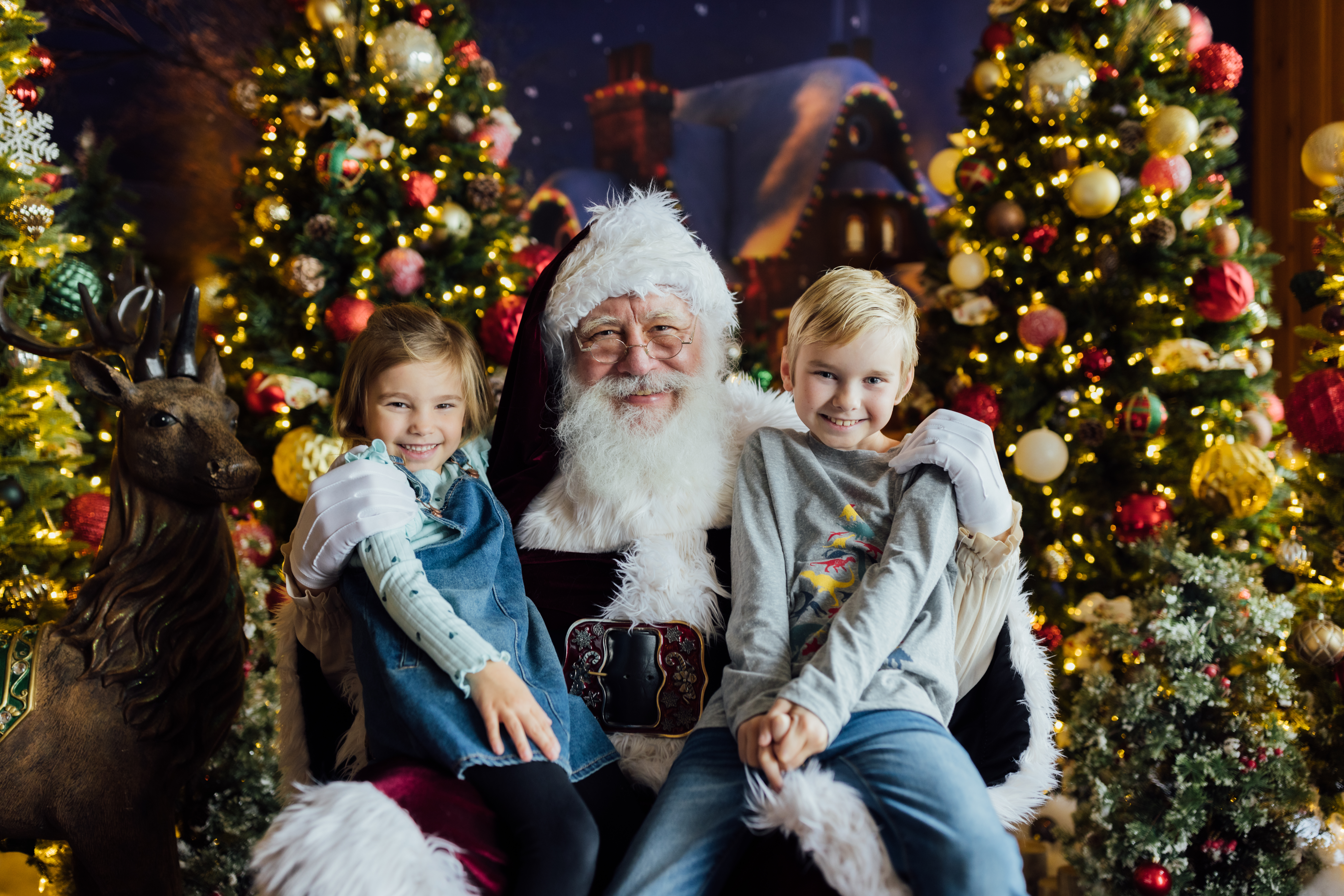 Two children sit on santa's lap, smiling