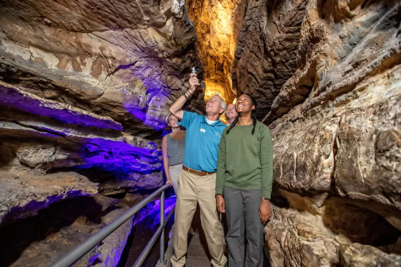 A tour guide shines a flashlight upward in the caves alongside a guest 