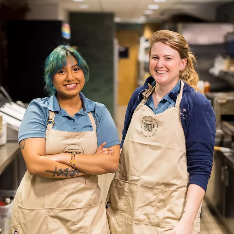 Two kitchen employees smile at the camera 