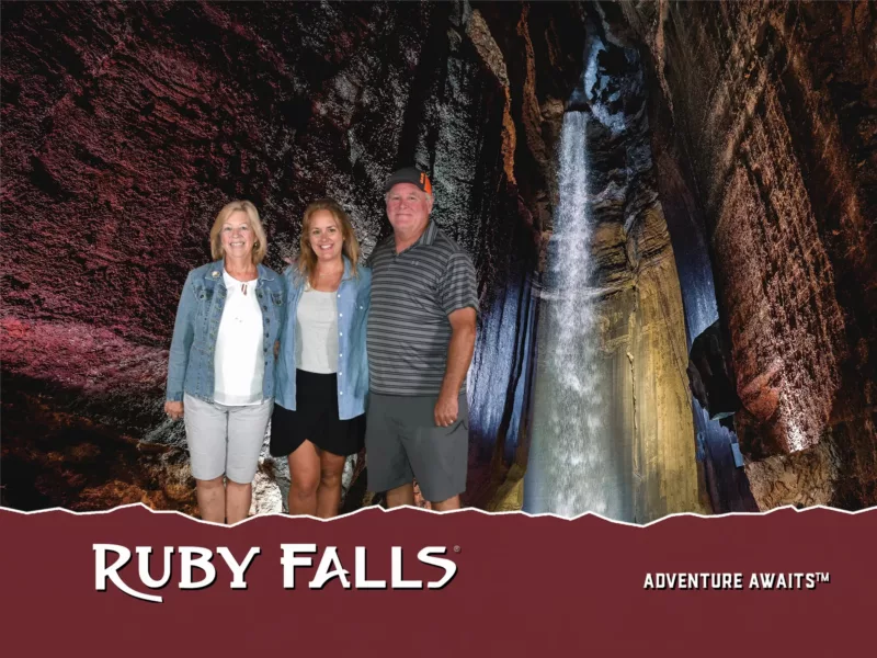 Two women and a man stand in a group in front of the Ruby Falls waterfall with the RF logo and 