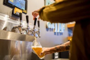 A cropped image of a person filling up a beer glass at a self-serve draft station 