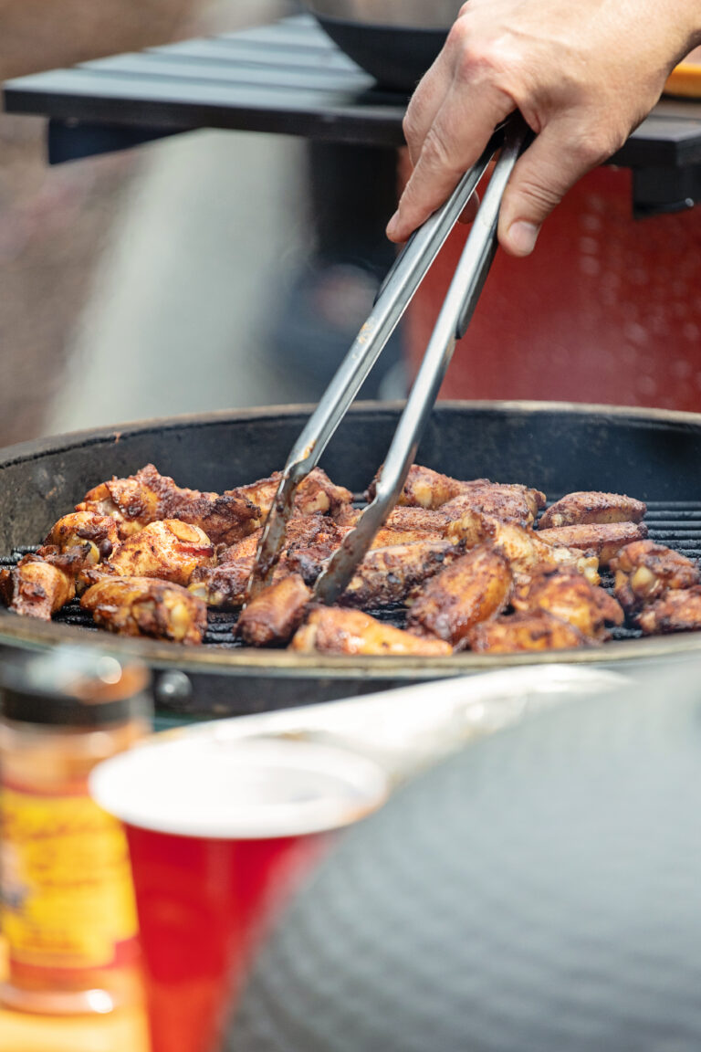 Hand using spatula to pick up grilled chicken wings on charcoal grill