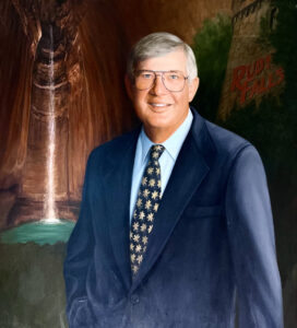 Painting of John Thomas Steiner, Sr. wearing a blue suit with blue shirt and tie stands in front of Ruby Falls waterfall and historic Lookout Mountain Tower.
