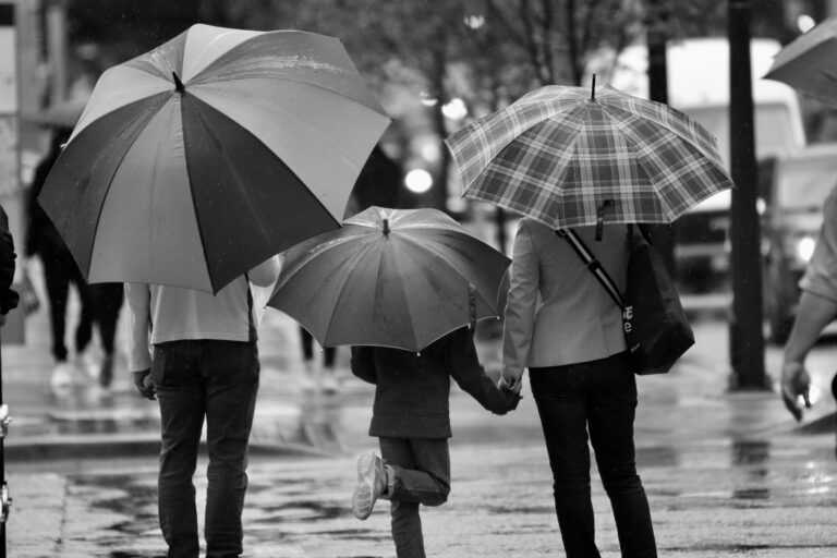 black and white photo of three people under umbrellas with the back toward the camera