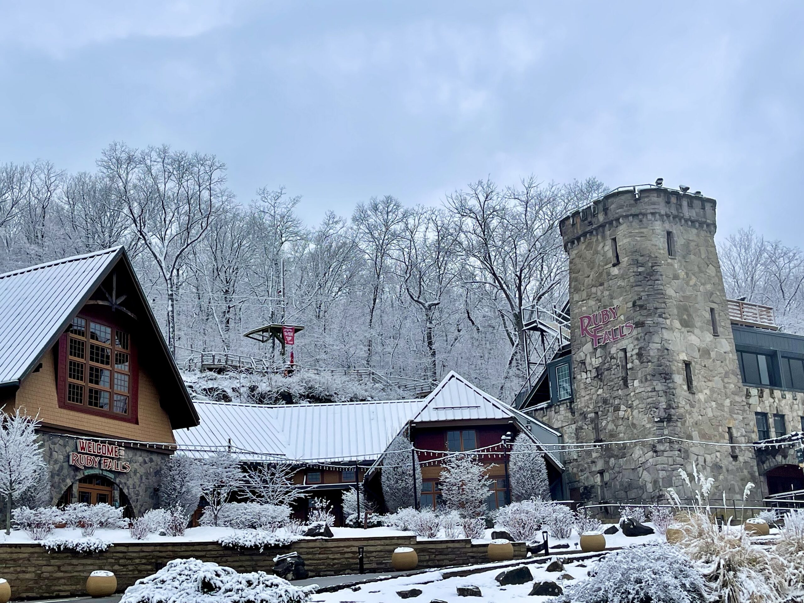 Snow covers the rooftops of the venues, ground and trees at Ruby Falls. The sky is cloudy and grey.
