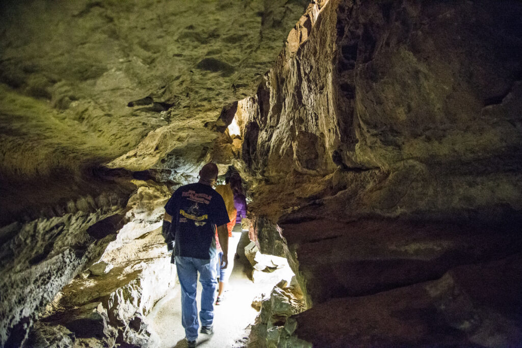 A man is facing away from the camera as he walks on the cavern trail in Ruby Falls Cave. He is surrounded by limestone.