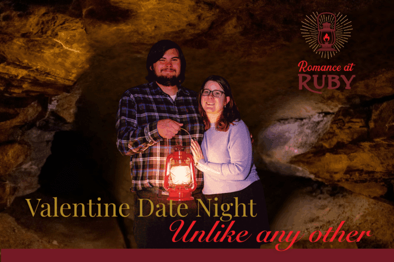 A man and woman stand side by side inside a cave. The man has one arm around the woman and he is holding a red lantern with his other hand.
